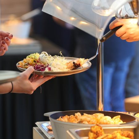 A buffet scene showing people serving assorted foods onto plates under warm lighting.